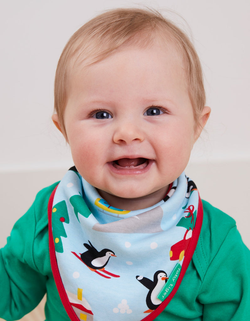 Toby Tiger Penguin Christmas Dribble Bib - A gorgeous bib in pale blue featuring sledging penguins and a sweet winter scene with a bold red trim. Sold by Say It Baby Gifts